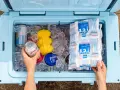 Hands packing a cooler with ice, cans, and reusable ice packs. This shows how to pack a cooler for a perfect picnic.