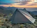 A Gossamer Gear tent sits on a rocky mountain ridge at sunset. This review highlights the gear's performance.