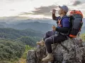 Backpacker drinks water on a rocky outcrop, contemplating how much water to bring backpacking for this stunning mountain vista.
