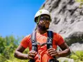 A man in a helmet and sunglasses pauses during a hike in hot weather, ready for his next climb.