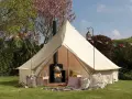 A cozy bell tent with a wood-burning stove inside, showcasing what is glamping: comfort and nature combined.