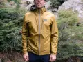 Man wearing a golden ultralight waterproof jacket with an OR logo, standing in a forest.