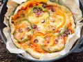 A delicious dutch oven pizza camping treat, topped with melted cheese, colorful bell peppers, and olives, baked to perfection on parchment paper.