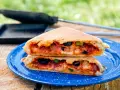 A delicious pie iron pizza, cut in half and stacked, reveals melted cheese, pepperoni, olives, and peppers.