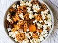 A bowl of delicious walnut trail mix, featuring popcorn, pretzels, dried cranberries, and apricots.