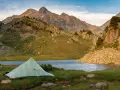 A tent sits by a serene lake, with rugged mountains in the background, a perfect campsite on the Pyrenees High Route.