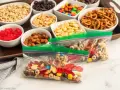 Bags of colorful trail mix bar ingredients: cereal, nuts, pretzels, candy, and dried fruit, ready for snacking.