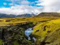 A winding path on the Laugavegur trail in Iceland leads past a mossy canyon with a cascading waterfall.