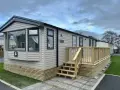 A beige Swift Provence mobil home with a wooden deck and steps. This idyllic location in Provence offers a cozy getaway.