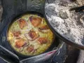 A delicious chicken and rice dish is cooking in a Dutch oven over a campfire, perfect for outdoor dutch oven campfire recipes.