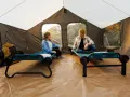 Two people relax on cots inside a large tent, showcasing smart tent camping hacks for comfort and organization.