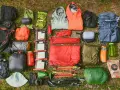 A comprehensive fastpacking gear list, including backpacks, sleeping bags, tents, jackets, food, and trekking poles, laid out on grass.