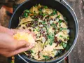 Making delicious camping nachos in a Dutch oven, adding shredded cheese to tortilla chips, black beans, and green onions.