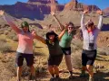 Four women pose with arms raised in a desert canyon, dressed for hiking in hot weather with shorts and light tops.
