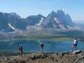 Three hikers enjoy a breathtaking view during their Tonquin Valley hike, with a stunning blue lake and jagged mountains behind them.