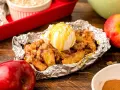 Warm campfire apples, baked in foil, topped with a scoop of vanilla ice cream and drizzled with caramel.