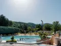 Enjoying a refreshing dip in the pool during a camping trip in Provence. Lush green hills and trees surround the sparkling water, with sun loungers and umbrellas ready for relaxation.