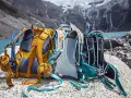 Three Osprey backpacks sit on rocks by a lake, ready for a hike. Learn how to pack a day pack for hiking with these essential tips.