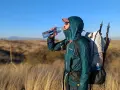 A hiker takes a refreshing drink from a Smartwater bottle while carrying a large backpack and trekking poles.