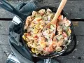 A hearty camping pasta dish with farfalle, zucchini, and tomatoes in a creamy sauce, served in a cast-iron skillet.
