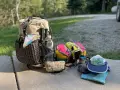 Ready for adventure! A large backpack, hiking poles, water bottle, and colorful pouches are laid out with camping gear, including a hat and gloves.