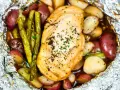 Campfire chicken foil packets in oven, with roasted potatoes and asparagus, seasoned with herbs.