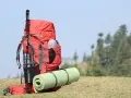 A red backpack with a rolled sleeping pad strapped to it, and trekking poles. This image shows how to pack a backpacking pack for an adventure.