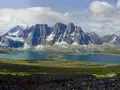 A vast mountain range with snow-capped peaks overlooks a serene blue lake. The Tonquin Valley Trail offers this breathtaking view of rugged beauty.