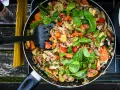 A colorful stir-fry with chicken, carrots, zucchini, and peppers, perfect for camp stove recipes. A black spatula is mixing the ingredients in a pan.