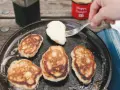 Frying pancakes in a cast iron skillet is a delicious answer to what to eat when camping. A fork lifts a fresh pancake, ready for syrup.