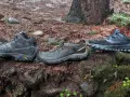 Three pairs of shoes on a wet forest floor: hiking boots, trail running shoes, and another pair of trail running shoes.