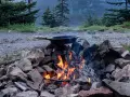 A cast iron skillet sits over a crackling campfire, ready for a delicious cast iron camping meal amidst a scenic mountain backdrop.