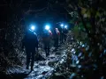 Hikers with headlamps navigate a dark, rocky trail, illuminated by their lights. These are some of the best night hiking tips.