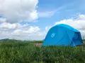A bright blue Nemo tent stands in a grassy field under a cloudy sky. This Nemo Aurora tent is ready for adventure.