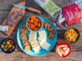 A delicious spread of camping snacks: sliced salami, cheese, crackers, dried apricots, olives, apple slices, and goldfish crackers.