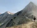 A hiker with a backpack and trekking poles walks along a narrow mountain ridge, a scenic path to learn how to get better at hiking.