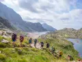 Hikers trek through a scenic mountain landscape, enjoying hiking the Pyrenees Spain. A chain of lakes and rugged peaks stretch into the distance under a cloudy sky.