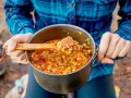 A wooden spoon scoops a hearty portion of campfire jambalaya from a pot.
