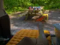 A person's legs rest on an orange sleeping pad inside a car. A picnic table with camping gear sits in a wooded area, ready for a road trip checklist.