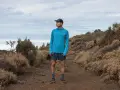 Runner in blue shirt and shorts on a dusty trail, contemplating the disadvantages of merino wool, like its tendency to hold moisture in humid conditions.