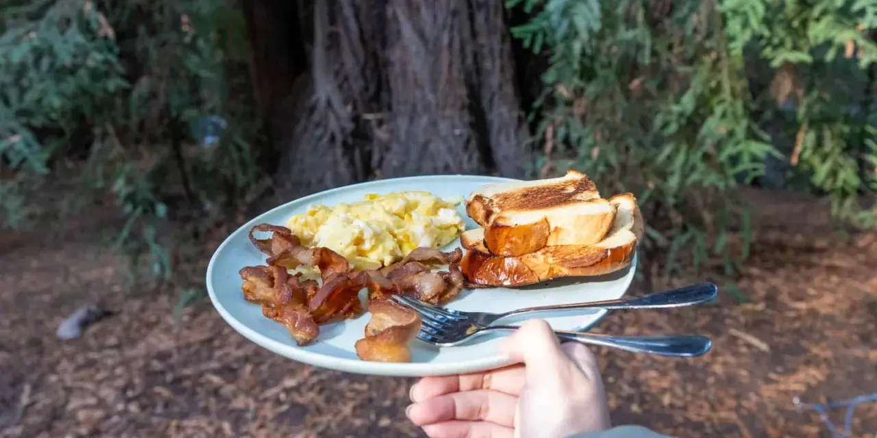 A plate of scrambled eggs, crispy bacon, and toasted bread, a delicious breakfast showcasing some great camping hacks for enjoying a hearty meal outdoors.