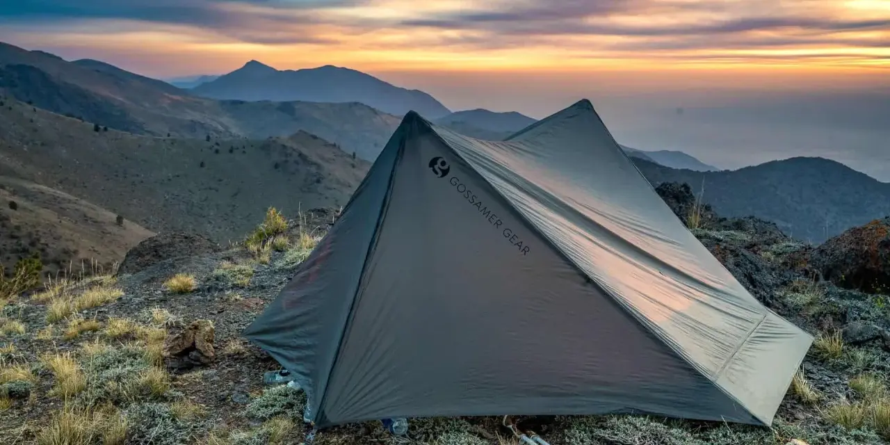 A Gossamer Gear tent sits on a rocky mountain ridge at sunset. This review highlights the gear's performance.