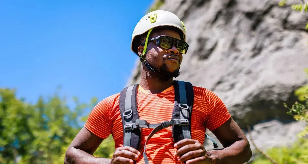 A man in a helmet and sunglasses pauses during a hike in hot weather, ready for his next climb.
