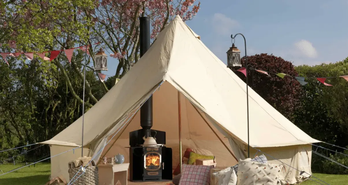 A cozy bell tent with a wood-burning stove inside, showcasing what is glamping: comfort and nature combined.