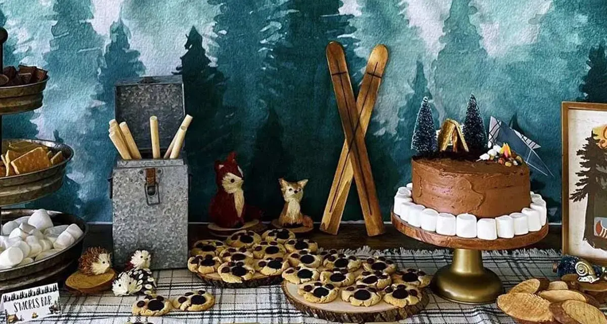 Woodland-themed camping party ideas: a chocolate cake with marshmallow border, s'mores supplies, cookies, and woodland creature decorations.