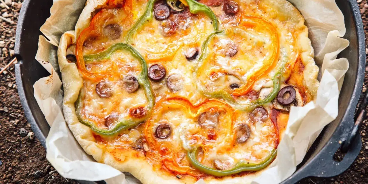 A delicious dutch oven pizza camping treat, topped with melted cheese, colorful bell peppers, and olives, baked to perfection on parchment paper.