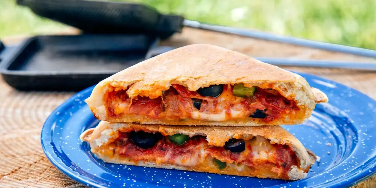 A delicious pie iron pizza, cut in half and stacked, reveals melted cheese, pepperoni, olives, and peppers.