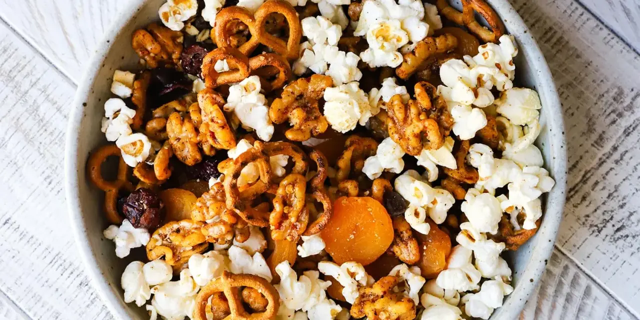 A bowl of delicious walnut trail mix, featuring popcorn, pretzels, dried cranberries, and apricots.