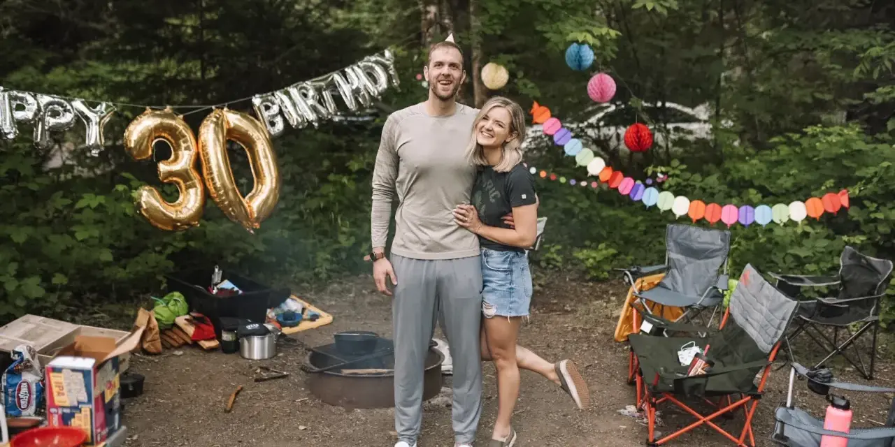 Couple celebrates 30th birthday with fun camping birthday ideas. Balloons and colorful banners decorate the campsite.
