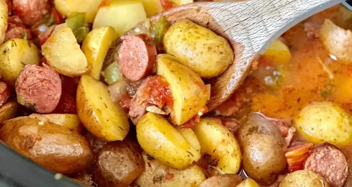 A wooden spoon scoops up hearty potatoes and sausage from a crockpot, perfect for camping crockpot meals.